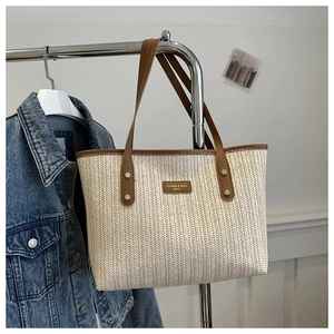 Détail de la texture du sac cabas en paille tissée avec anses en cuir sur un cintre