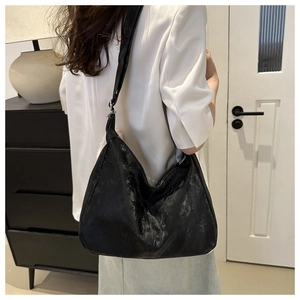 Detail view of a black crescent shoulder bag with glossy crinkle texture on a model