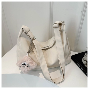 Detail of off-white oversized hobo bag with wide shoulder strap and plush charm