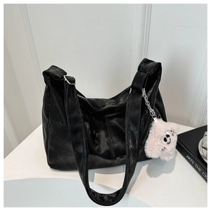 Detailed view of large black velvet shoulder bag with plush bear pendant on white stand