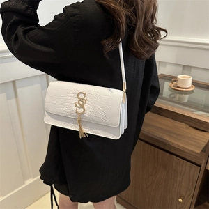 White faux crocodile skin shoulder bag with gold letter logo and tassel charm on model
