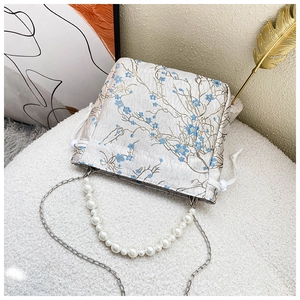 Detail of vintage beige bucket bag with blue floral embroidery and pearl handle strap