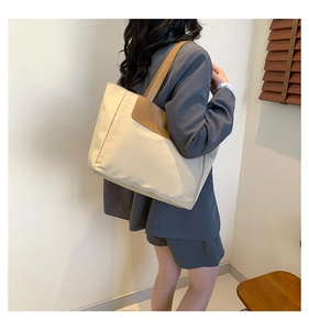 Detail of a beige canvas tote bag with brown PU leather straps worn by a model