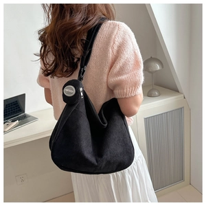 Detail view of a large black corduroy tote bag with round coin purse and logo badge