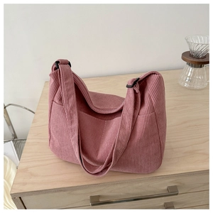 Pink corduroy tote bag detail showing vertical ribbed texture and side pocket on wood