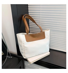 Close-up of contrast stitching on white nylon tote bag with brown leather handles