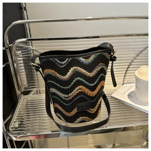 Detail of colorful wavy embroidery on a black bucket bag featuring a Fashion metal plaque