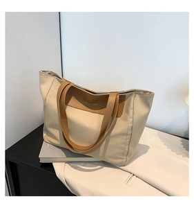 Detail of minimalist cream tote bag with brown leather handles and golden fashion text