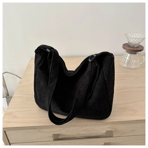 Detail of black corduroy hobo bag with zip closure on minimalist wood surface