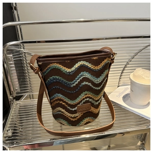 Close-up of brown bucket bag with colorful wavy embroidery and smooth leather trim details