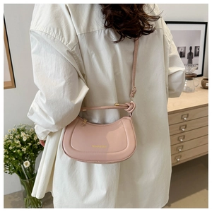 Pale pink crescent bag in glossy patent leather styled in a cozy indoor setting