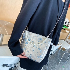 Silver satin crossbody bag with blue floral embroidery, pearl handle, and chain strap
