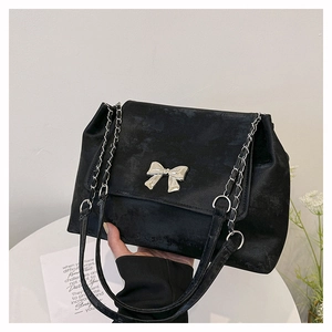 Detail of black suede bag with a large silver butterfly buckle and leather chain strap