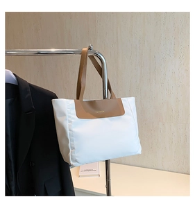 Detail of white fabric tote bag with brown leather accents and gold fashion logo