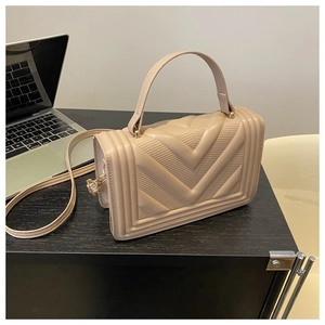 Dettaglio borsa a tracolla beige trapuntata con trama a V su scrivania in legno scuro