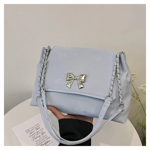 Detail of light blue suede shoulder bag featuring a silver bow metal piece and chain strap