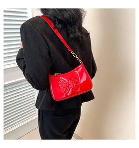 Sac rouge verni avec relief papillon 3D porté sur une veste de tailleur noire