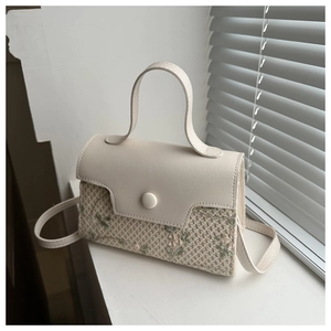 Detail of small woven crossbody bag with beige faux leather flap and floral embroidery