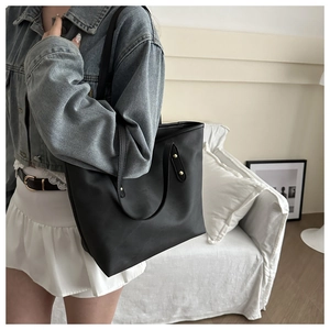 Detail of a large black minimalist leather tote bag with elegant gold studs for women