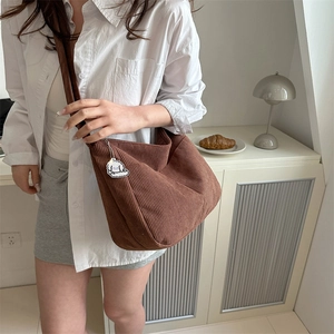 Brown corduroy hobo bag with wide shoulder strap and cloud pendant worn by a model