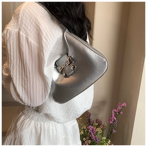 Silver metallic underarm bag with metal bow detail worn over a white dress