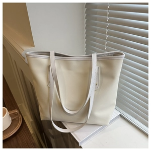 Close-up of cream leather tote bag with gold rivets on a desk with coffee and books