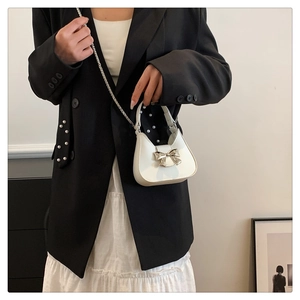 Detail of white patent leather shoulder bag with silver bow buckle and chain strap