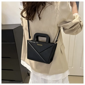 Detail of black geometric fold shoulder bag featuring gold Fashion text and top handle