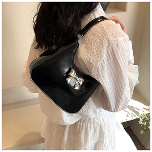 Close-up of black glossy leather shoulder bag featuring a silver metal bow buckle detail