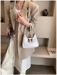 Detail of white crescent underarm bag featuring a golden metal bow buckle and chain strap