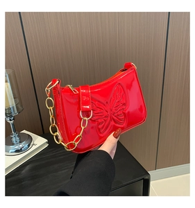 Détail du sac bandoulière en cuir verni rouge avec motif papillon gaufré en relief