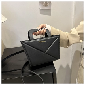 Close-up of black crossbody bag with geometric fold design and gold fashion text detail