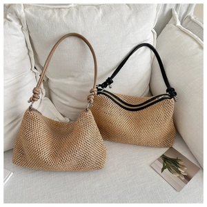 Detailaufnahme der Strohtasche mit schmalen Lederriemen und Knotendetails auf dem Sofa
