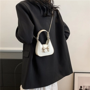 White half-moon crossbody bag with silver bow accent and metallic chain strap worn by model
