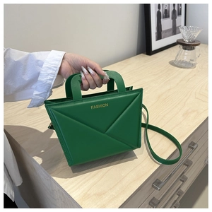 Close-up of green crossbody bag with geometric pleated lines and metal fashion logo