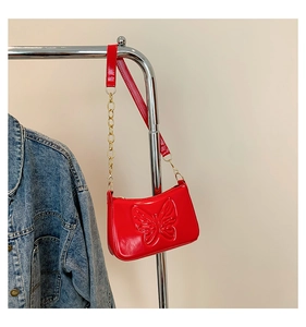 Détail du sac rouge en cuir verni avec motif papillon embossé et chaîne dorée chic