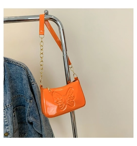 Détail macro du sac en cuir verni orange avec papillon gaufré et chaîne en métal