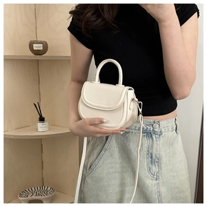Detail of a white mini PU leather saddle bag with top handle and slender shoulder strap