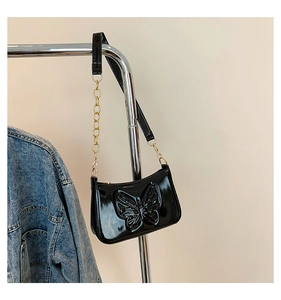 Détail du motif papillon en relief sur sac bandoulière en cuir verni noir avec chaîne dorée