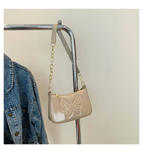 Détail du papillon embossé sur sac en cuir verni beige avec bandoulière en chaîne dorée