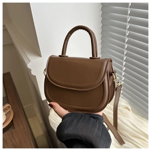 Close-up of a deep brown mini saddle bag with fine leather texture and metal hooks