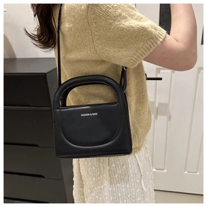 Detail of black crossbody bag with white letter print and textured rectangular shape