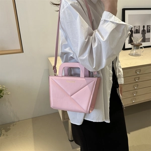 Pink crossbody handbag with geometric texture and gold lettering shown with a model