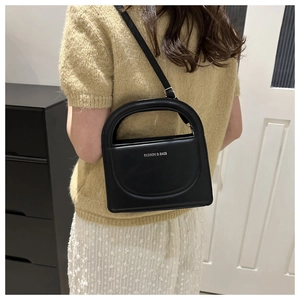 Detail of black crossbody bag featuring a D-shaped handle and silver fashion lettering