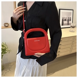 Detail of red leather square bag featuring a unique hollow handle and fashion lettering