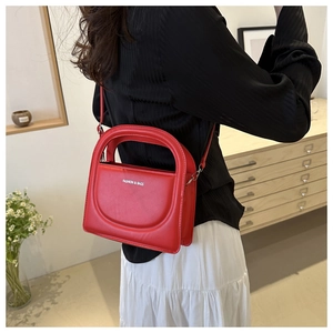 Detailed view of a red leather crossbody bag with rounded handle and logo detail
