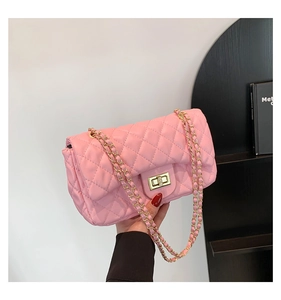 Close-up of pink quilted crossbody bag with gold metal clasp and chain strap held by model