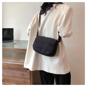 Détail d'un sac bandoulière noir matelassé avec large sangle sur une tenue de bureau