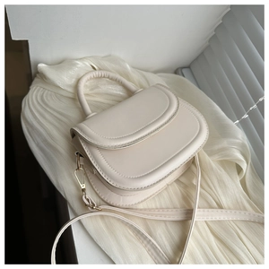 Close-up of minimalist beige crossbody bag with top handle and gold metal hardware