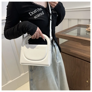 Detail of a creamy white crossbody bag with Fashion & Bags logo and curved stitching